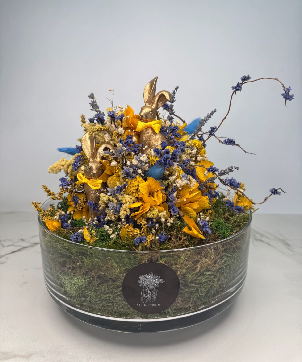 Trockenblumenarrangement in Blau- und Gelbtönen, platziert in einer eleganten zylindrischen Glasvase.