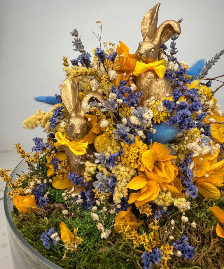 Nahaufnahme eines Trockenblumenarrangements in Blau- und Gelbtönen, platziert in einer eleganten zylindrischen Glasvase.